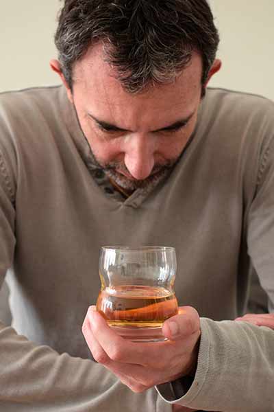 грустный мужчина держит перед собой стакан с алкоголем